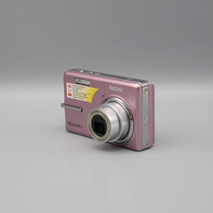 Pink Kodak EasyShare M1073 IS viewed from a front angle with its lens extended and top controls visible.