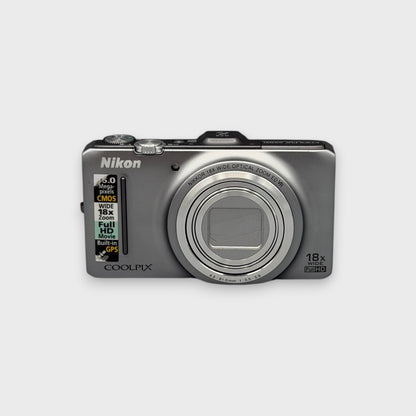 Front view of a silver Nikon Coolpix S9300 digital camera with its lens closed