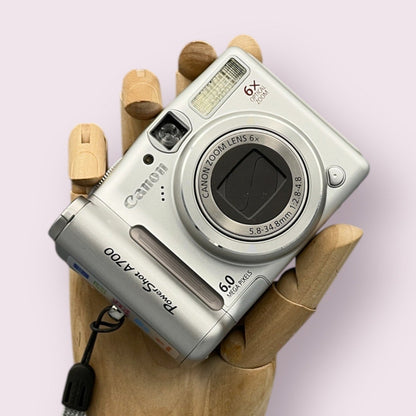 Silver Canon PowerShot A700 digital camera resting in a wooden hand with the lens closed