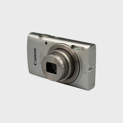 Silver Canon PowerShot ELPH 180 viewed from a front angle showing its extended lens and side panel.