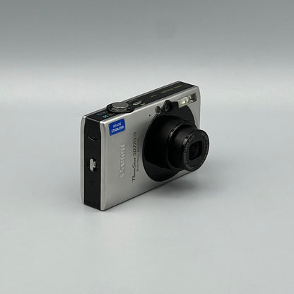 Angled front view of a silver Canon PowerShot SD770 IS showing its extended lens and black side panel
