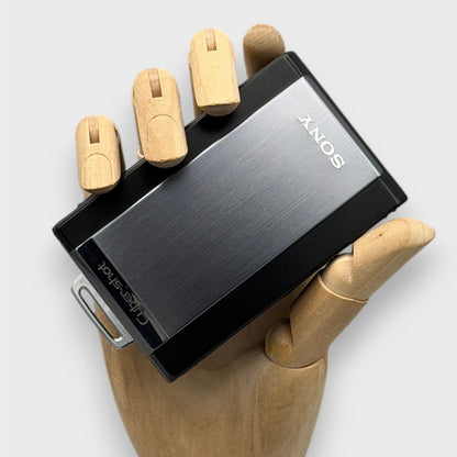 Gray and black Sony Cyber-shot DSC-T300 digital camera resting in a wooden hand with its sliding lens cover closed