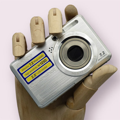 Silver Sony Cyber-shot DSC-S750 with its lens closed and a yellow feature sticker, held in a wooden display hand