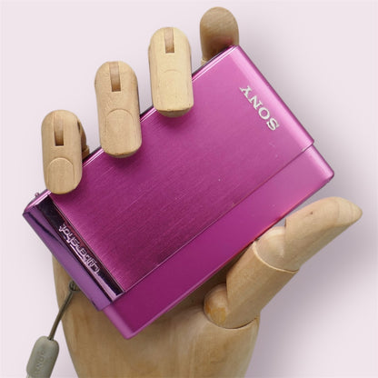 Pink Sony Cyber-shot DSC-T90 digital camera resting in a wooden hand with its sliding lens cover closed