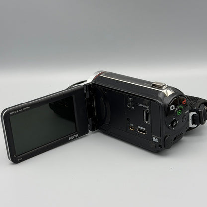 Sanyo Xacti VPC-FH1 camcorder with its screen open, showing the memory card slot and side ports