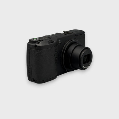 Angled front view of a black Ricoh GR Digital showing the extended lens and top controls