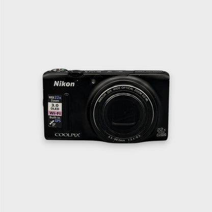 Front view of a black Nikon Coolpix S9500 digital camera with its lens closed