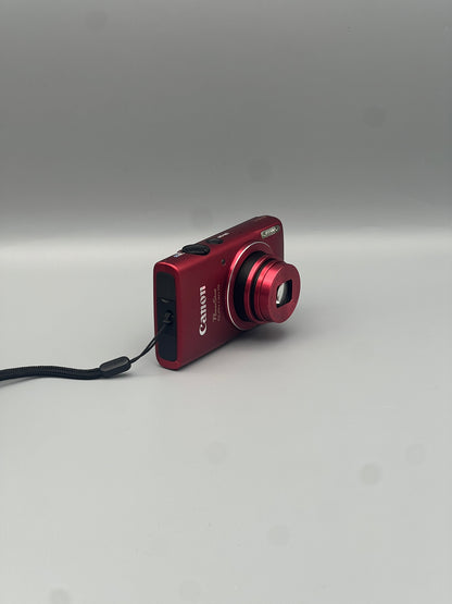 Angled front view of a red Canon PowerShot ELPH 130 IS showing its extended lens and black side panel