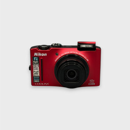 Front view of a red Nikon Coolpix S8100 with its black lens extended and flash raised