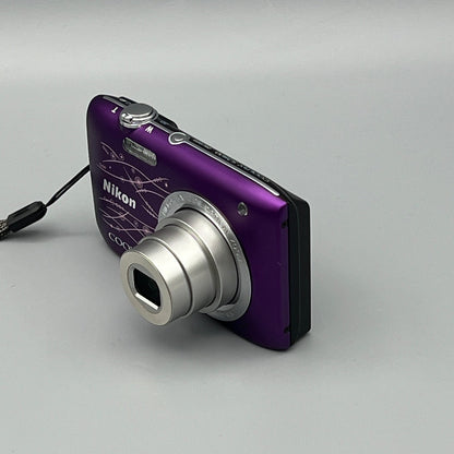 Purple Nikon Coolpix S2800 viewed from a front angle showing the extended lens, patterned body and top controls.