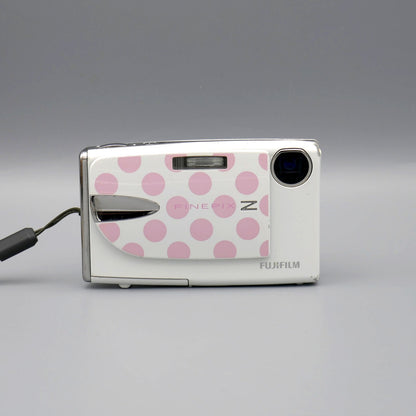 Front view of a white Fujifilm FinePix Z20fd with its pink polka-dot lens cover open