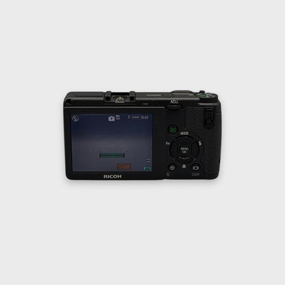 Rear view of a black Ricoh GR Digital showing the illuminated LCD screen and control buttons