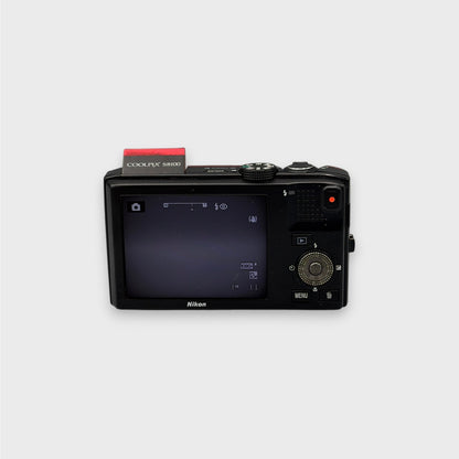 Rear view of a red Nikon Coolpix S8100 showing its LCD screen, black back panel, control dial and raised flash
