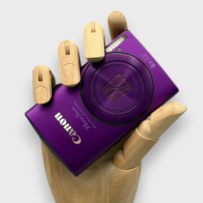 Purple Canon PowerShot ELPH 310 HS digital camera resting in a wooden hand with the lens closed