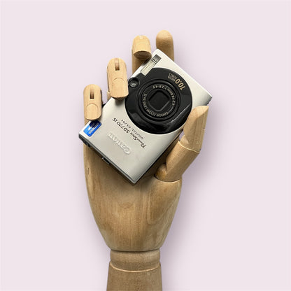 Silver Canon PowerShot SD770 IS with its lens closed, held in a wooden display hand