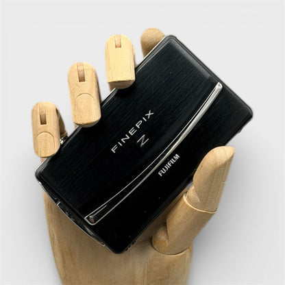Black Fujifilm FinePix Z90 digital camera resting in a wooden hand with its sliding lens cover closed