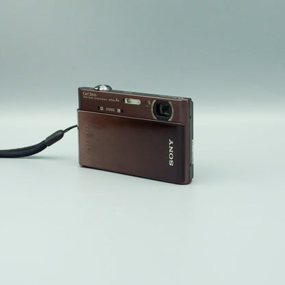 Brown Sony Cyber-shot DSC-T900 viewed from the opposite front corner with its lens cover open