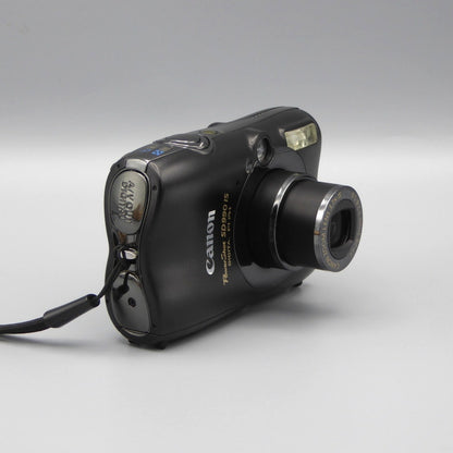 Angled front view of a black Canon PowerShot SD990 IS showing the extended lens and top controls