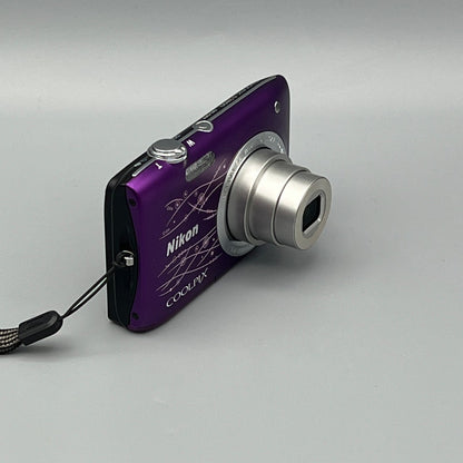 Purple Nikon Coolpix S2800 viewed from a front angle showing the extended silver lens and wrist strap.