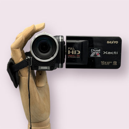 Black Sanyo Xacti VPC-FH1 camcorder held in a wooden display hand with the flip-out screen open