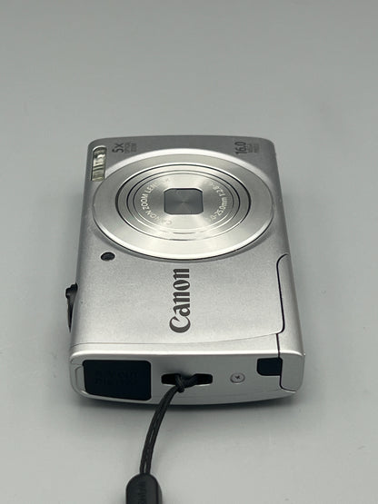 Silver Canon PowerShot A2500 lying flat with its lens closed and wrist strap attachment visible
