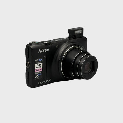 Angled front view of a black Nikon Coolpix S9500 with its lens extended and flash raised