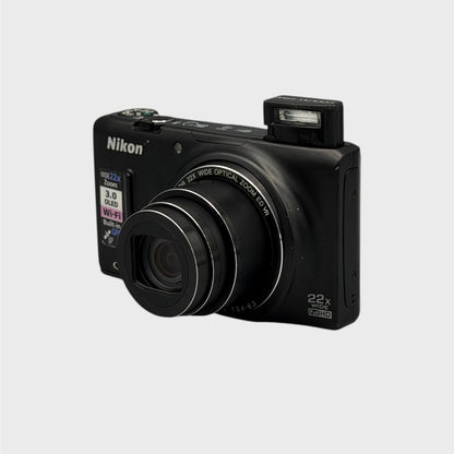 Front and side view of a black Nikon Coolpix S9500 with its lens extended and flash raised