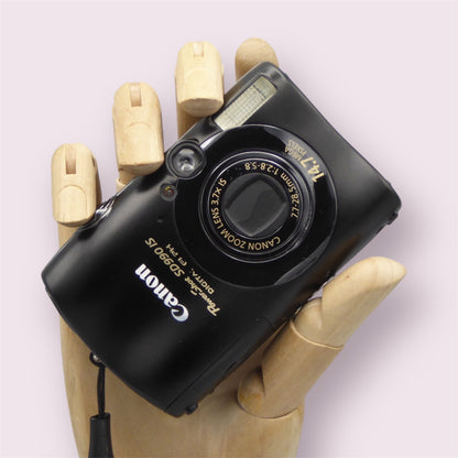 Black Canon PowerShot SD990 IS digital camera resting in a wooden hand with the lens closed