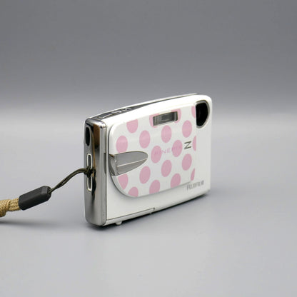 Angled front view of a white Fujifilm FinePix Z20fd showing its pink polka-dot cover and wrist strap attachment