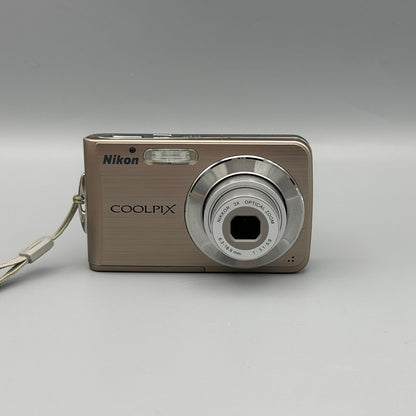 Bronze Nikon Coolpix S210 front view with its silver lens extended and wrist strap attached.