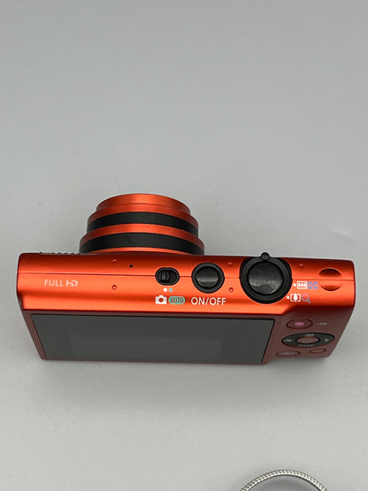 Top view of a red Canon PowerShot ELPH 110 HS showing its extended lens, shutter button and power button