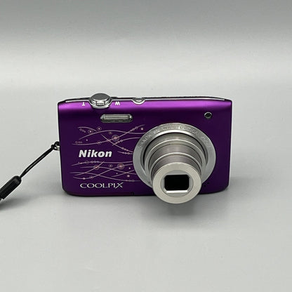 Purple Nikon Coolpix S2800 front view showing its decorative line pattern and extended silver lens.