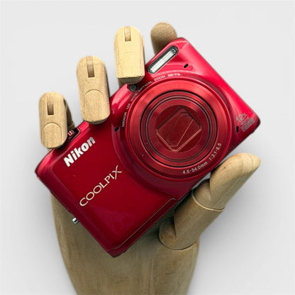 Red Nikon Coolpix S6500 held in a wooden display hand with its lens closed.