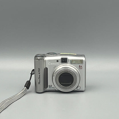 Front view of a silver Canon PowerShot A700 digital camera with closed lens and wrist strap