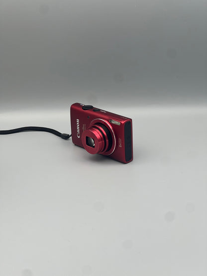 Red Canon PowerShot ELPH 130 IS viewed from the opposite front corner with its lens extended
