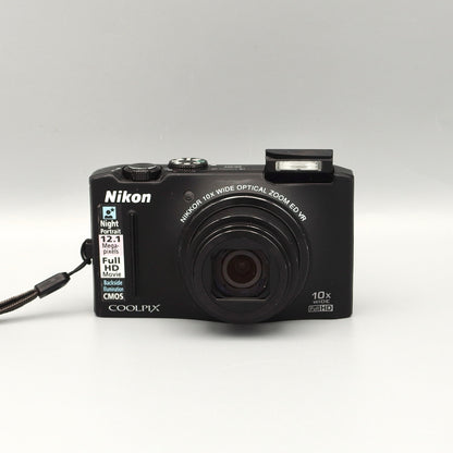 Black Nikon Coolpix S8100 front view with its lens extended and pop-up flash raised.
