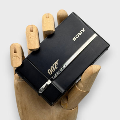 Black Sony Cyber-shot DSC-T50 with a gold 007 logo and closed lens cover, held in a wooden display hand