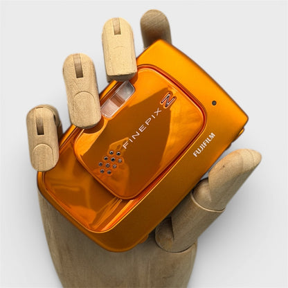 Orange Fujifilm FinePix Z30 held in a wooden display hand with its sliding lens cover closed.