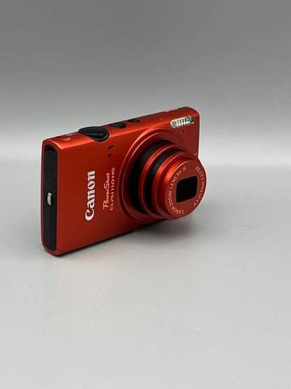 Angled front view of a red Canon PowerShot ELPH 110 HS showing its extended lens and black side panel
