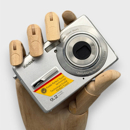 Silver Kodak EasyShare M320 with its lens closed, held in a wooden display hand