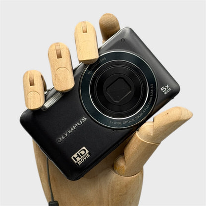 Black Olympus VG-120 with its lens closed, held in a wooden display hand
