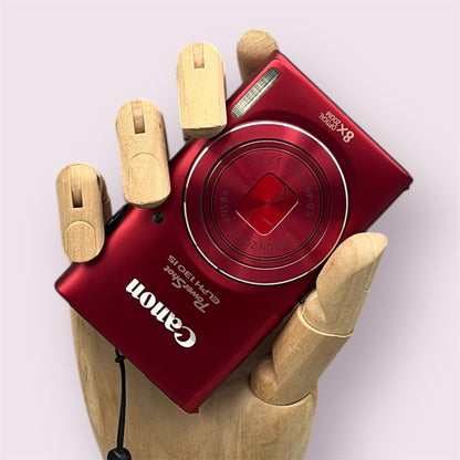 Red Canon PowerShot ELPH 130 IS with its lens closed, held in a wooden display hand