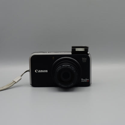 Front view of a black Canon PowerShot SX210 IS with its lens extended and flash raised
