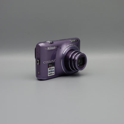 Purple Nikon Coolpix S6400 viewed from a front angle showing its extended lens and side panel.