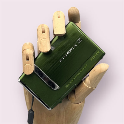 Green Fujifilm FinePix Z10fd held in a wooden display hand with its sliding lens cover closed.