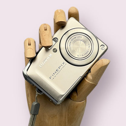 Silver Fujifilm FinePix F50FD held in a wooden display hand with its lens closed.