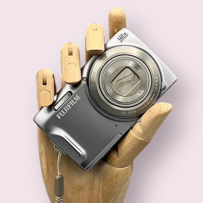 Silver Fujifilm FinePix T550 digital camera resting in a wooden hand with the lens closed