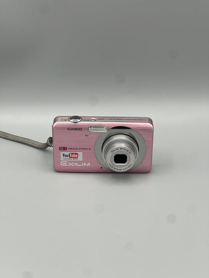 Pink Casio Exilim EX-Z85 front view with its silver lens extended and wrist strap attached.