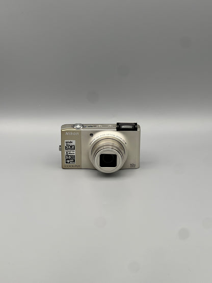 Front view of a silver Nikon Coolpix S8000 with its lens extended and pop-up flash raised