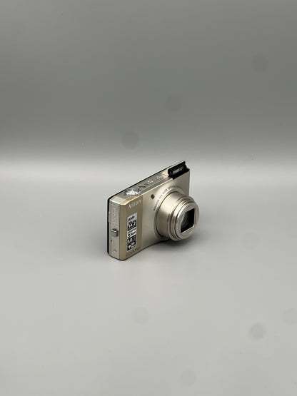 Angled front view of a silver Nikon Coolpix S8000 showing its extended lens and raised flash